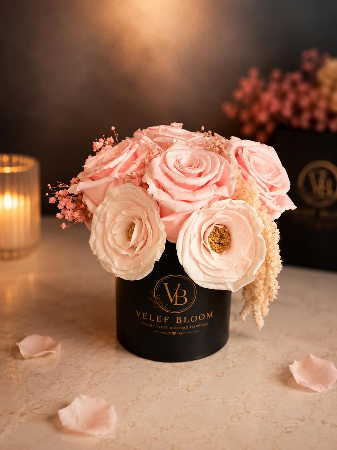 Petite arrangement of blush and champagne preserved roses and ranunculus in a black Velef Bloom ceramic vessel, lit by candlelight