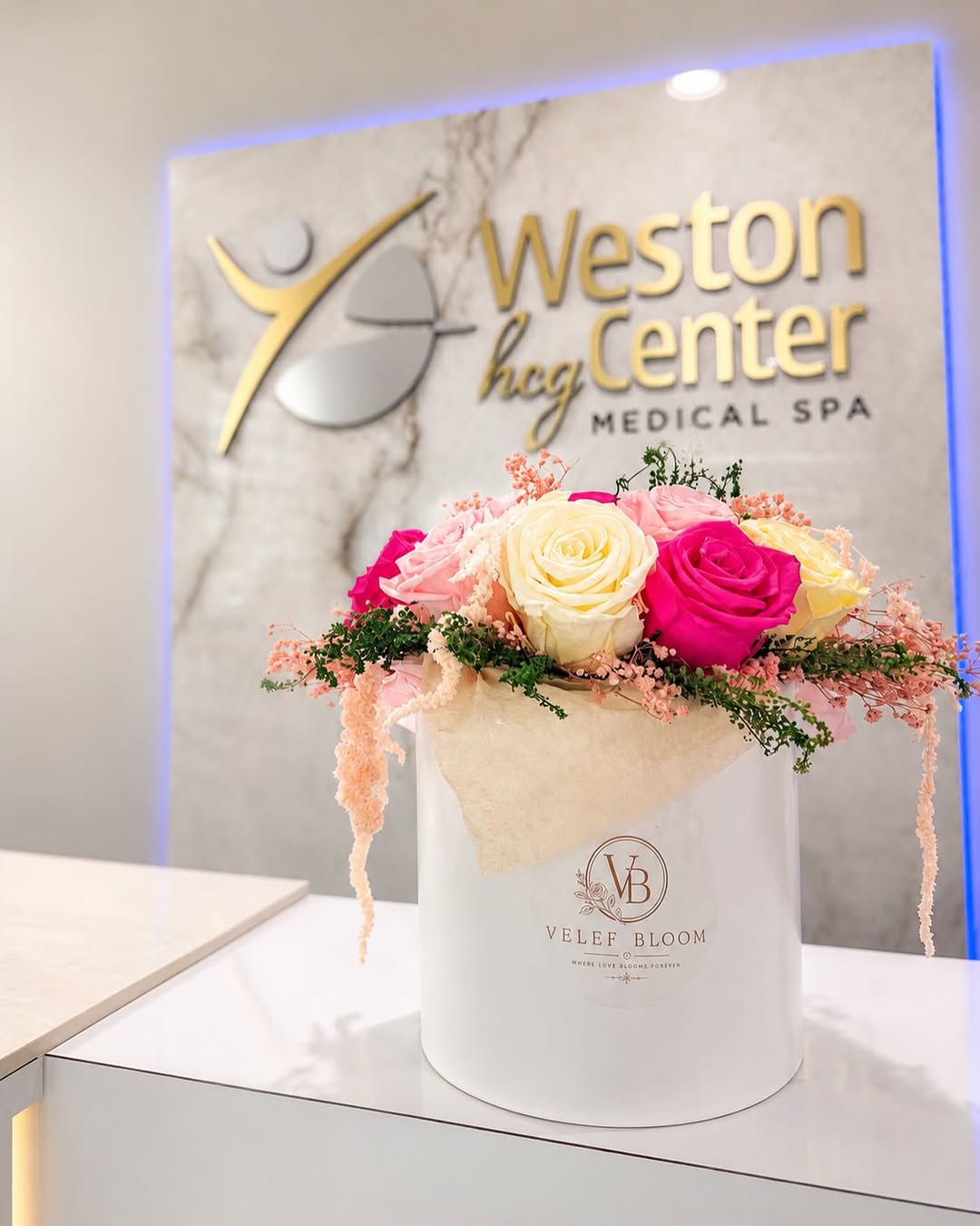 A white Velef Bloom arrangement of hot pink, cream and yellow preserved roses at the Weston HCG Center reception