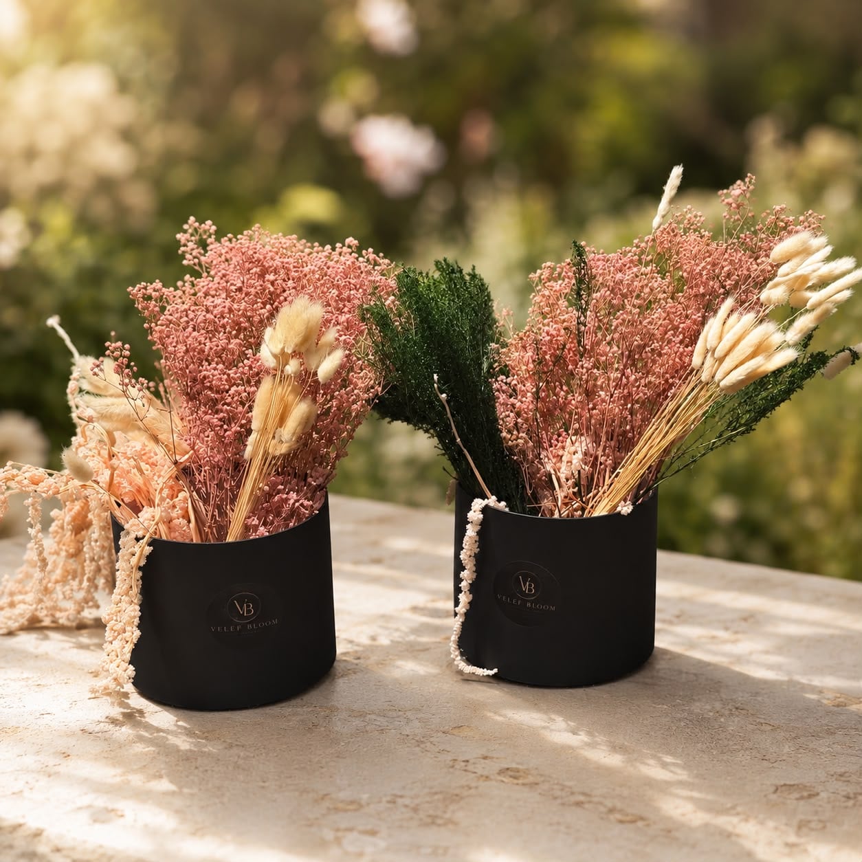 Two black Velef Bloom vessels filled with blush preserved gypsophila and dried accents, on a stone table