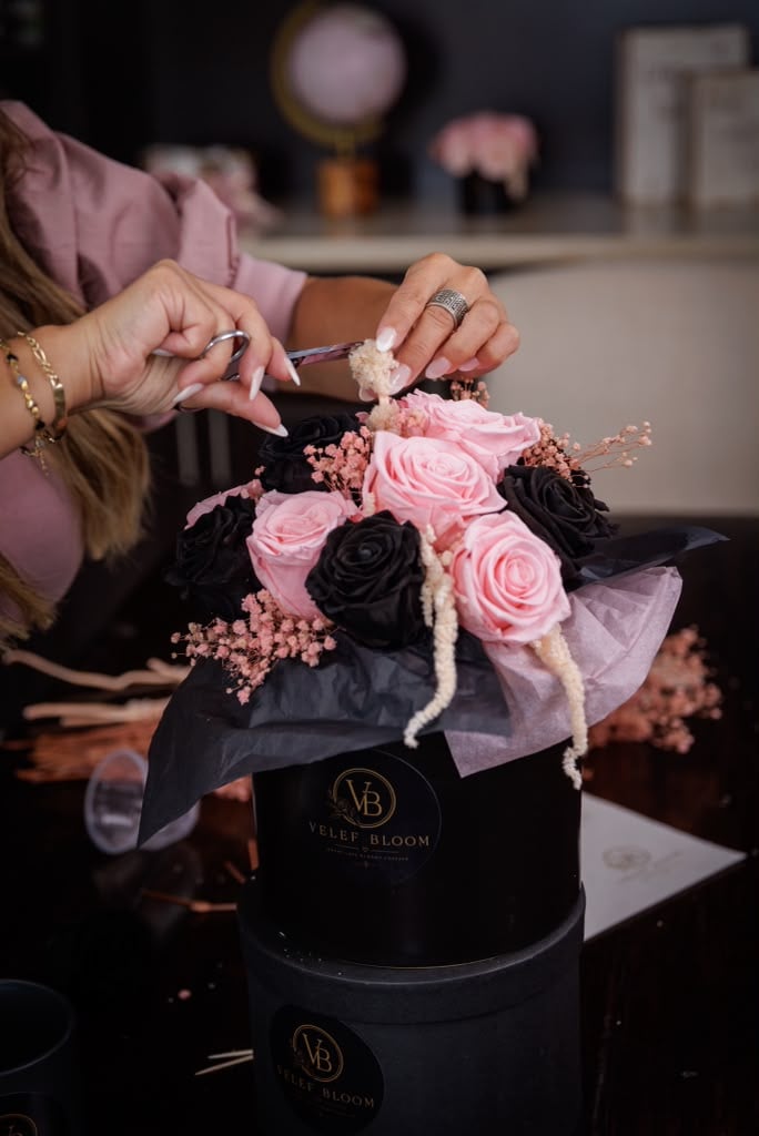 Hands finishing a black and blush preserved rose arrangement inside a black Velef Bloom box lined with tissue